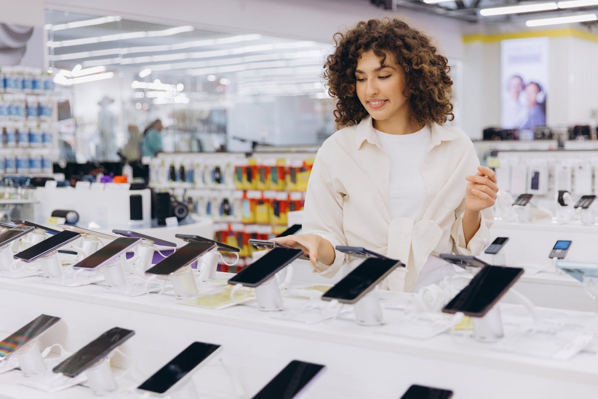 Customer comparing new smartphones in an electronics store, choosing the best mobile phone for her needs. Electronics business lease solicitors help retailers secure the right premises.