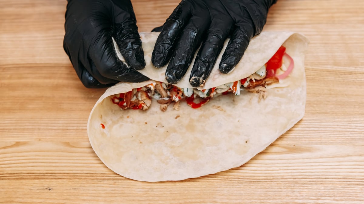 Chef preparing food in a takeaway kitchen, wrapping flatbread with chicken vegetables and sauce